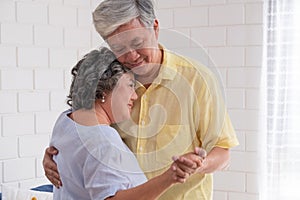 Happy Asian senior couple enjoy slow dancing at living room in house with warm love emotion.grandmother snuggle grandfather