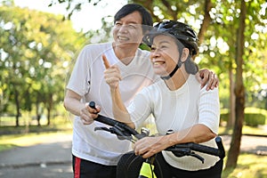 Happy Asian senior couple riding bicycles at summer park. Active retirement lifestyle concept.