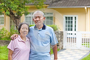 Happy asian senior couple standing in front of a house