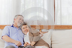 Happy Asian senior couple stay together on sofa at home in romantic moment. Retired lovely elderly smiling grandparent lover