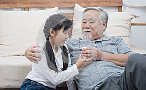 Happy asian senior elderly grandfather have grandchild look after and take care with giving milk and kiss on cheek while sitting