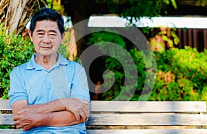 Happy asian senior gentleman sitting on a wooden bench and relaxing in a park  on a sunny day