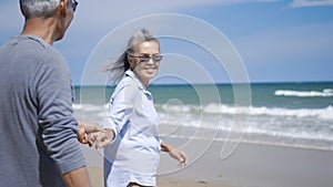 Senior man and woman couple holding hands walking to the beach sunny with bright blue sky