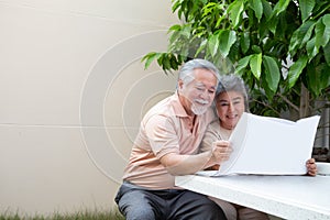 Happy Asian senior mature couple reading newspaper at front garden home