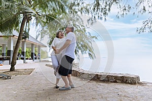 Happy asian senior retired couple, relax smiling elder man and woman enjoying with retired vacation at sea beach outdoor. Health