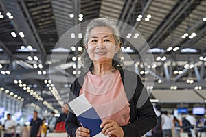 happy asian senior woman with grey hair holding passport and boarding pass in the airport