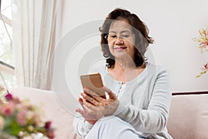 Happy Asian senior woman sitting on sofa and using a smart phone