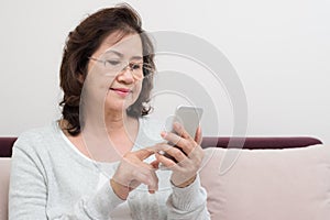 Happy Asian senior woman sitting on sofa and using a smart phone