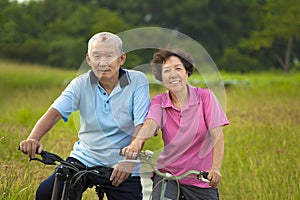 Happy Asian seniors couple biking in Park.