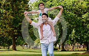 Happy asian single father carrying daughter on his shoulders in the park. Smiling man and child pretending they can fly