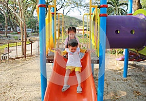 Happy asian sister and her little brother enjoy playing slider in playground in the park. Child girl play with her brother outdoor