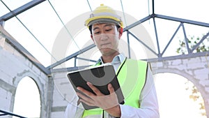 Happy Asian smiling in engineering uniform at construction site while holding a tablet.