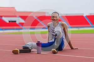 Happy Asian speed runner, with two prosthetic running blades, enjoys a restful moment on the stadium track after a rigorous speed