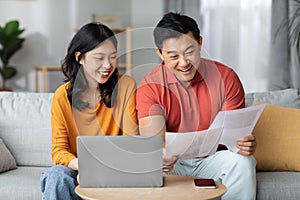 Happy asian spouses paying bills online, using laptop