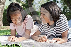 Happy Asian student while lying read book on the blanket in the summer, Asia two girl smile and relaxation together at park in the