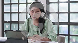 Happy Asian student women wearing headphones and using a digital tablet to listening relax music in a library