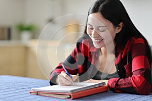 Happy asian student writing notes on notebook at home