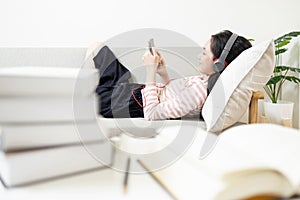 Happy asian teenage girl wearing headphones lying on the couch,resting and listening to music online on mobile phone,enjoy and