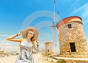 Asian traveler girl posing near famous Rhodes attraction - old windmills. Vacation in Greece concept