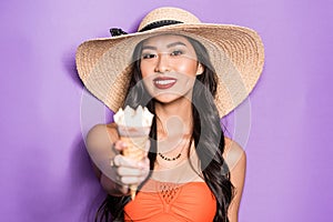 happy asian woman in beach attire holding out an ice-cream cone and looking