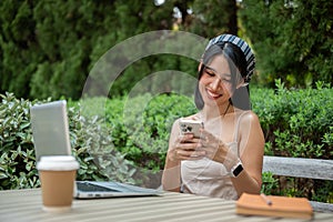 A happy Asian woman chats with her friends on her phone while working remotely in the garden