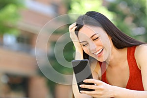 Happy asian woman checking phone message in the street