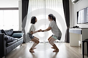 Happy asian woman and child girl holding hands together while workout,doing sumo squat exercise at home,have fun,laugh,enjoy on