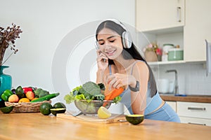A happy Asian woman enjoys the music while preparing ingredients for her healthy breakfast