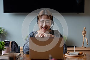 Happy asian woman freelancer wearing headset, communicating with client via video computer call. Millennial pleasant