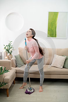 Happy asian woman in headphones with mop and bucket cleaning floor and singing at home