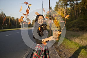 Happy Asian woman holding autumn leaves in nature on sunny day.