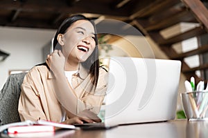 Happy asian woman laughing, working on laptop from home. Girl student studying on computer, online learning, remote