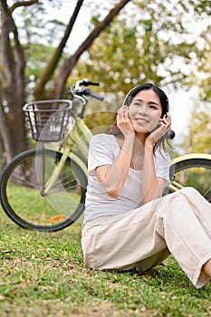 Happy Asian woman listening to music and taking a rest after cycling in the public park