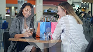 Happy asian woman looking at a new dress, her blond friend take photo of her in shopping mall