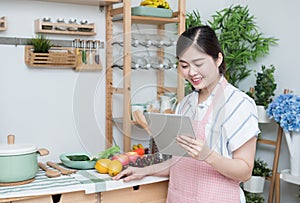 Happy asian woman looking recipe tablet kitchen reading cooking at home,University colleague student study online with social