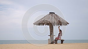 Happy asian woman open arms happily under straw umbrella on tropical beach. copy space provided. travel concept. woman taking deep