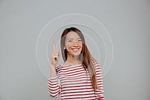 Happy asian woman pointing finger up at copy space