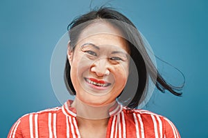 Happy Asian woman portrait against blue background - Senior Chinese female having fun posing in front of camera