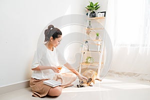 Happy Asian woman reading a book and sitting on floor with her black dog at home, lifestyle concept