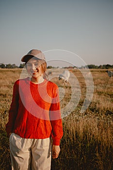 Happy asian woman in red sweater walks on the grass field to see the cows cattle and the sunset view.