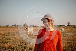 Happy asian woman in red sweater walks on the grass field to see the cows cattle and the sunset view.