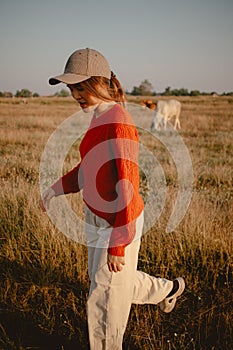 Happy asian woman in red sweater walks on the grass field to see the cows cattle and the sunset view.