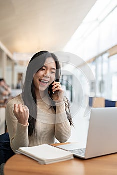 A happy Asian woman rejoicing after receiving good news over the phone