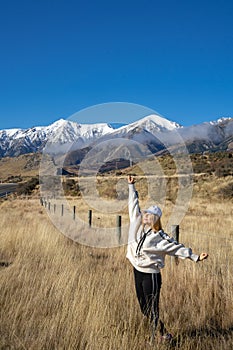 Happy asian woman relaxing on dried grass, blue sky with sunlight at sunny winter day, travel vacation, landscape snow mountains