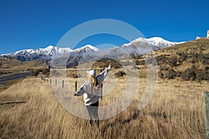 Happy asian woman relaxing on dried grass, blue sky with sunlight at sunny winter day, travel vacation, landscape snow mountains