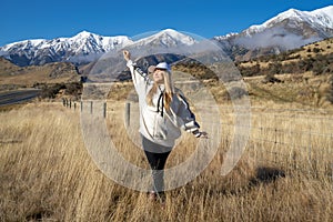 Happy asian woman relaxing on dried grass, blue sky with sunlight at sunny winter day, travel vacation, landscape snow mountains