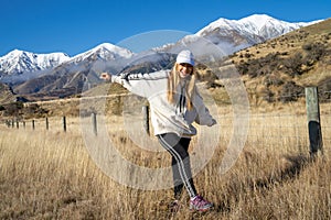 Happy asian woman relaxing on dried grass, blue sky with sunlight at sunny winter day, travel vacation, landscape snow mountains