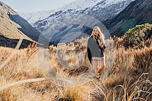 Happy asian woman relaxing on dried grass, blue sky with sunlight at sunny winter day, travel vacation, landscape snow mountains