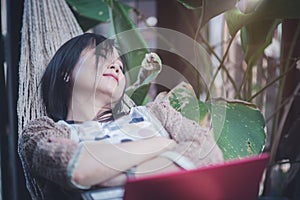 Happy asian woman relaxing in a hammock after working online with a laptop placed on top of her.Concept of relaxation in nature