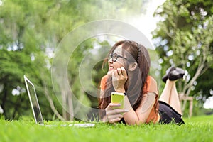 Happy Asian woman resting and looking beside in park with smartphone. People and lifestyles concept. Technology and Beauty theme.